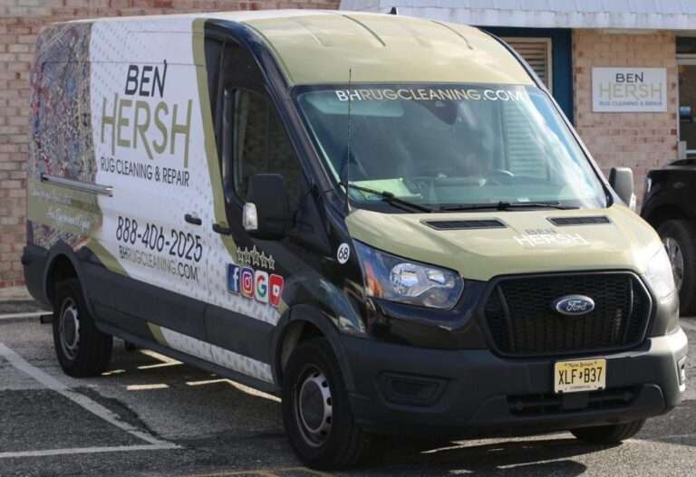 A white and green Ford van from one of the best rug cleaning companies near me, Ben Hersh Rug Cleaning & Repair, is parked in a lot. Sporting their logo and branding, it features "rug repair near me," phone number 888-406-2255, and website barugcleaning.com on its side and hood against a brick backdrop.